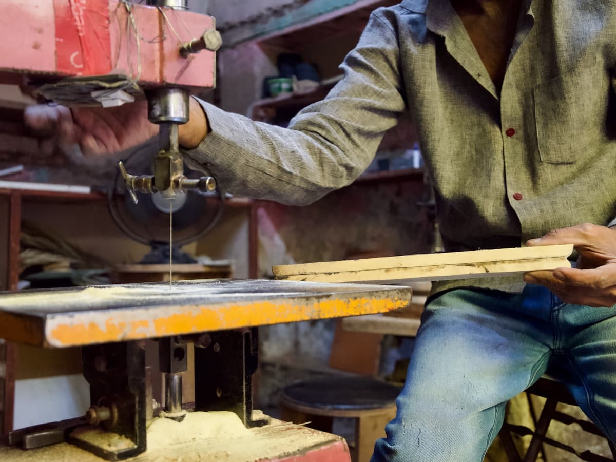 A maker guiding a wooden board through a scroll saw in a workshop