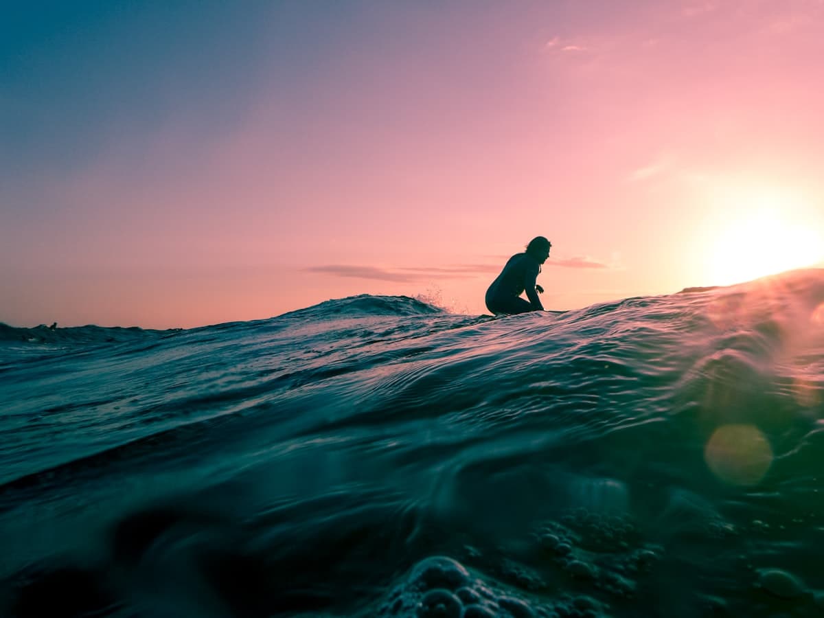 A surfer paddling over a glassy wave at golden hour